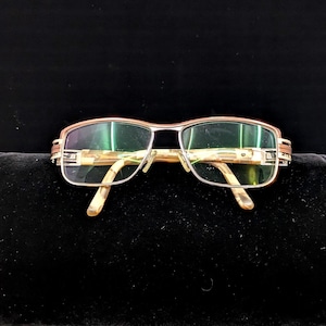 May include: Rectangular eyeglasses with a gold and silver metal frame. The temples feature a decorative pattern. The clear lenses are set in the frame, and the arms have a patterned design.