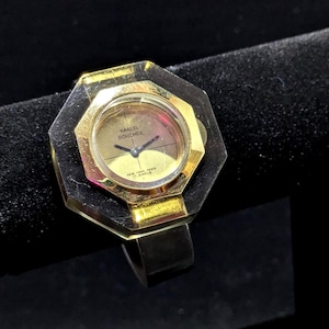 Può includere: Orologio vintage Marcel Boucher con quadrante ottagonale dorato e cinturino nero. Il quadrante dell'orologio ha lancette dorate e la scritta "Marcel Boucher New York - Paris 17 Jewels". Un gioiello unico.