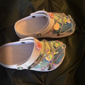 Puede incluir: Un par de zuecos blancos personalizados con parches de mezclilla, pedrer&iacute;a y adornos coloridos. Los zuecos est&aacute;n decorados con flores rosas y naranjas, detalles de cuentas y dijes de piruletas. La hora 13:54 est&aacute; visible en la esquina inferior.