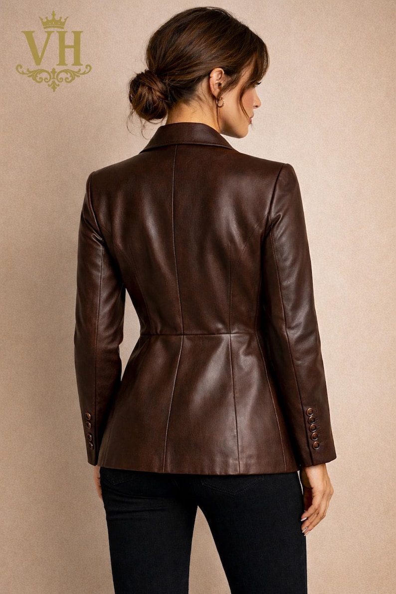 May include: A brown leather blazer with long sleeves and a tailored fit. The blazer has a button closure on the sleeves and a classic collar. The back view shows the blazer's design and stitching details. The logo "VH" is visible in the upper left corner.