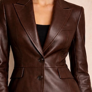 May include: A brown leather blazer with a classic tailored design. The jacket features a notched lapel, two front pockets, and two buttons. The blazer is a rich, dark brown color and appears to be made of high-quality leather.