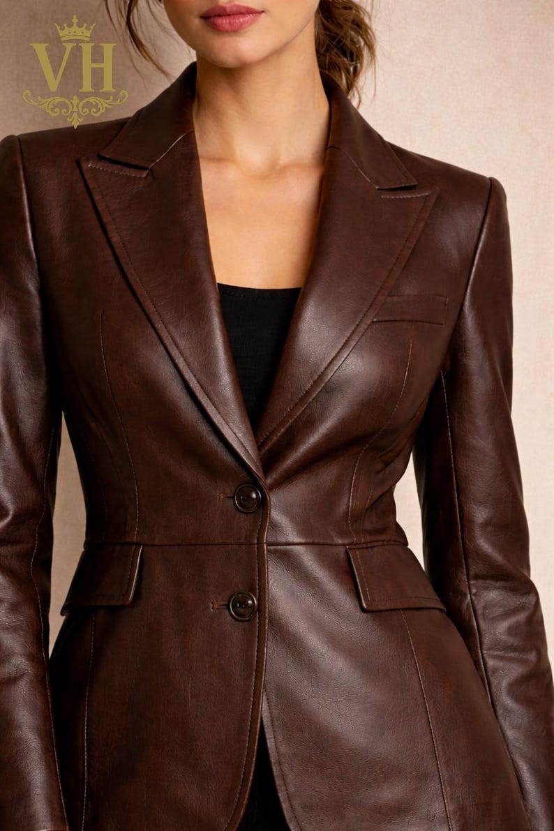 May include: A brown leather blazer with a classic tailored design. The jacket features a notched lapel, two front pockets, and two buttons. The blazer is a rich, dark brown color and appears to be made of high-quality leather.