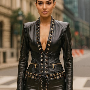 May include: Black leather jacket and pants set with gold-colored accents. The jacket features a plunging neckline, gold grommets, and a corset-style closure. The pants have a lace-up detail at the waist. The outfit is from Vintage HideCo.