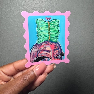May include: A pink sticker featuring a cartoon illustration of a person with a stack of green money on their head. The person has blue eyes and the word "Hustler" is on their forehead. A pink heart is above the money stack.