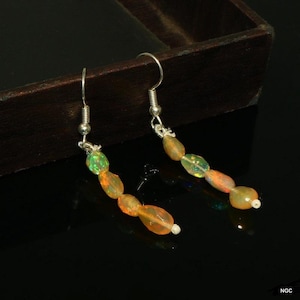 May include: A pair of drop earrings featuring silver-toned fishhook wires and a vertical arrangement of four multi-colored, translucent, oval-shaped opal beads. The beads display iridescent flashes of green, orange, and yellow hues throughout.