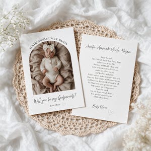 May include: Two white rectangular cards with black text and a photo of a baby. One card features an arched photo of a baby in a white onesie and bow, with the text Auntie Amma & Uncle Mason and Will you be my Godparents? The other card contains a poem.