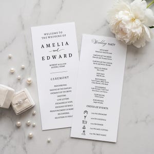 Op de afbeelding: Twee witte trouwprogramma-kaarten met zwarte tekst die de ceremonie en de bruiloftsgasten voor Amelia en Edward op 30 oktober 2026 in Austin, Texas, beschrijven. De kaarten bevatten een lijst met evenementen met iconen en een ringdoosje.