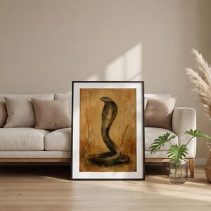 May include: A framed wall art print featuring an oil painting of a cobra snake in a defensive posture. The snake is rendered in dark brown and black tones against a textured, warm ochre and tan background with vertical brushstrokes and grass.