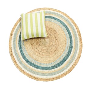 May include: A round, woven jute rug featuring concentric circles in natural tan, white, and teal blue. A square throw pillow with vertical lime green and white stripes is placed on top of the rug, creating a layered, textured visual composition.