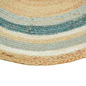 May include: A circular rug constructed from braided natural fibers, featuring concentric rings of tan, light blue, and white. The texture is coarse and woven, displaying a repeating pattern of these three distinct colors in a circular arrangement.