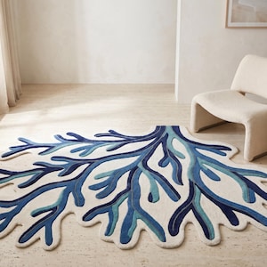 May include: An area rug with an irregular, organic shape resembling a coral reef. The rug features a cream-colored base with a layered, branching design in various shades of blue, including navy, royal blue, and light turquoise accents.