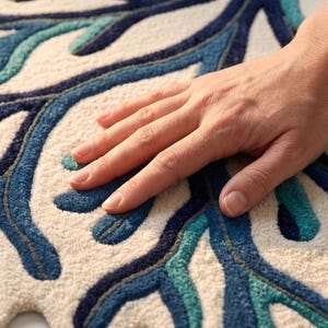 May include: A tufted rug featuring a cream-colored base with a raised, branching pattern in shades of navy blue, royal blue, and teal. The design consists of organic, flowing lines that mimic coral or tree branches with a thick, textured pile.