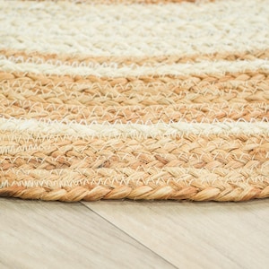 May include: A round braided rug featuring concentric circles of natural tan jute and off-white fibers. The texture is created by thick, tightly woven strands that form a repeating pattern of alternating light and neutral earth-toned bands.