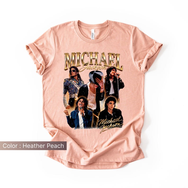 May include: Heather peach-colored t-shirt featuring a collage of Michael Jackson images. The shirt has the text "Michael Jackson" in gold lettering. The images show Jackson in various poses, wearing different outfits.