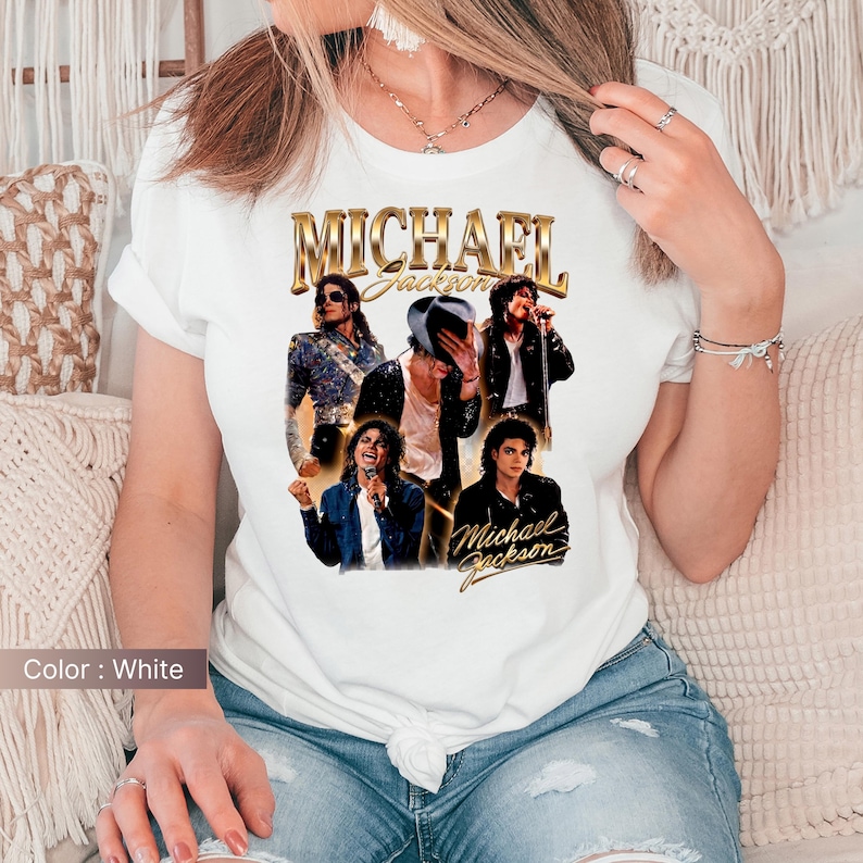 May include: White t-shirt featuring a collage of images of Michael Jackson, with the name "MICHAEL JACKSON" in gold lettering. The shirt showcases various poses of the artist, capturing his iconic style and performances.