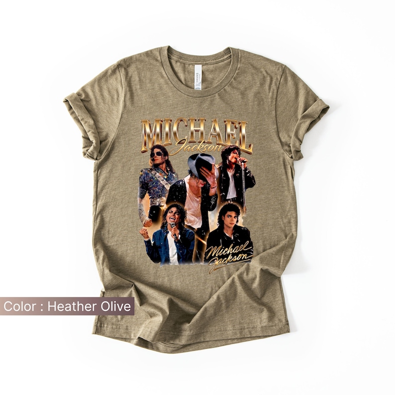 May include: Heather olive-colored t-shirt featuring a collage of images of Michael Jackson. The design includes the name "Michael Jackson" in a gold, vintage-style font. The shirt showcases various poses of the singer.