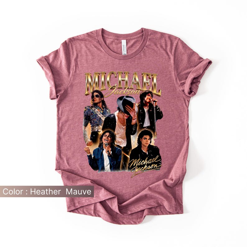 May include: Heather mauve t-shirt featuring a collage of Michael Jackson images. The design includes the name "Michael Jackson" in gold lettering. The images show Jackson in various poses and outfits, with a vintage aesthetic.