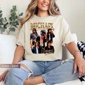 May include: Sand-colored t-shirt featuring a collage of images of Michael Jackson, with the name "MICHAEL JACKSON" in gold lettering. The shirt showcases various poses of the artist, creating a vintage aesthetic. The color of the shirt is sand.