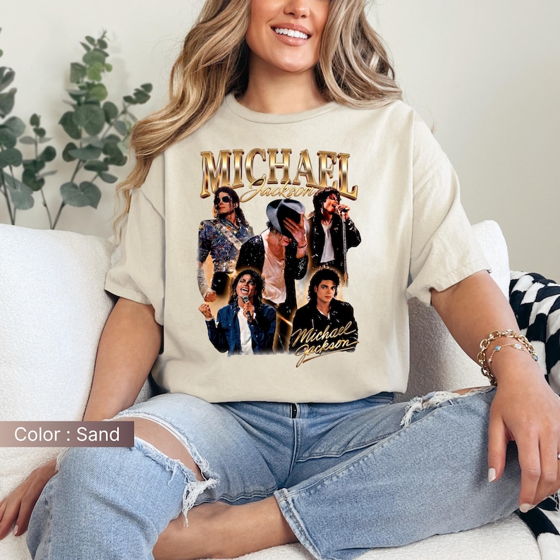 May include: Sand-colored t-shirt featuring a collage of images of Michael Jackson, with the name "MICHAEL JACKSON" in gold lettering. The shirt showcases various poses of the artist, creating a vintage aesthetic. The color of the shirt is sand.