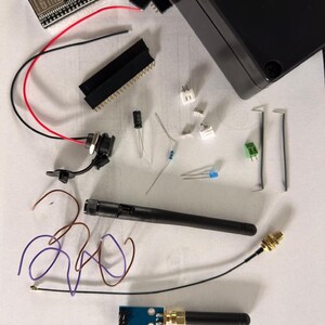 May include: A collection of electronic components, including a circuit board, wires, connectors, and a black antenna. The items are laid out on a white surface, possibly for a DIY electronics project or kit.