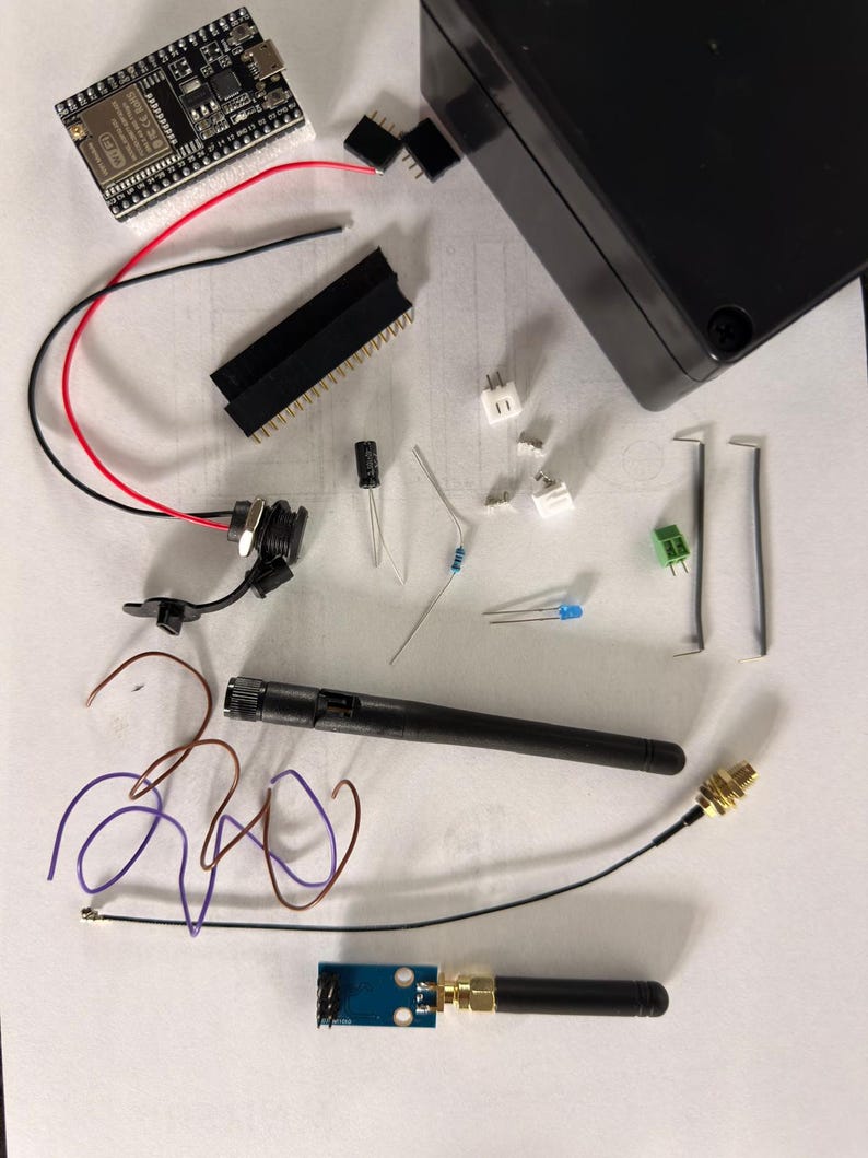 May include: A collection of electronic components, including a circuit board, wires, connectors, and a black antenna. The items are laid out on a white surface, possibly for a DIY electronics project or kit.