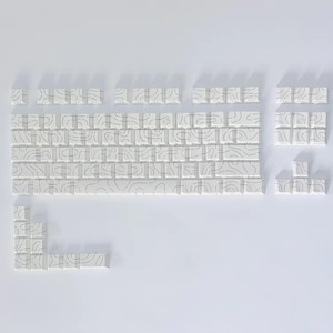 May include: A set of white keyboard keycaps featuring a black topographic line pattern. The keycaps are arranged to display a keyboard layout, with keys of various sizes and shapes. The design is minimalist and contemporary.