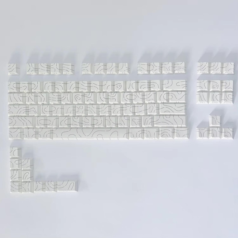 May include: A set of white keyboard keycaps featuring a black topographic line pattern. The keycaps are arranged to display a keyboard layout, with keys of various sizes and shapes. The design is minimalist and contemporary.