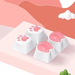 May include: Four white keyboard keycaps with pink paw prints and paw shapes. The keycaps are arranged on a pink surface with a soft, pastel background. The keycaps are a cute and playful design.