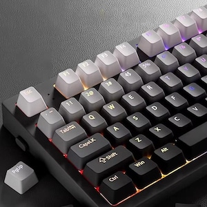 Puede incluir: Primer plano de un teclado mecánico con marco negro y teclas grises y negras. Las teclas están dispuestas en una distribución QWERTY estándar, con teclas de función en la parte superior. El teclado tiene un diseño moderno y minimalista.