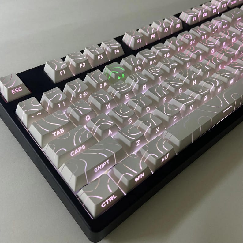 May include: A mechanical keyboard with white keycaps and a distinctive swirling pattern. The keys are illuminated with a soft pink light, and the keyboard has a black frame. The layout includes keys such as ESC, TAB, SHIFT, and CTRL.