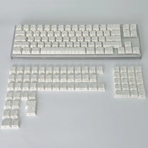 May include: A white mechanical keyboard with keycaps featuring a topographic design in grey. The keyboard is shown with extra keycaps. The keys have various labels, including letters, numbers, and function keys.