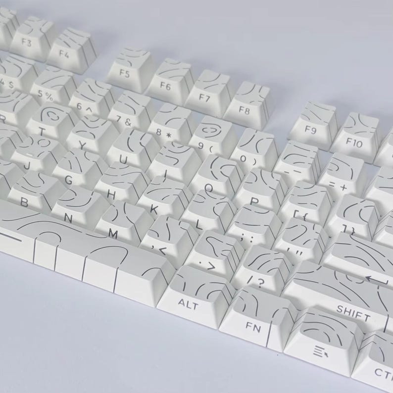 May include: A white mechanical keyboard with keycaps decorated with a black, abstract pattern. The keyboard includes function keys, letters, numbers, and symbols. The keys are arranged in a standard QWERTY layout.