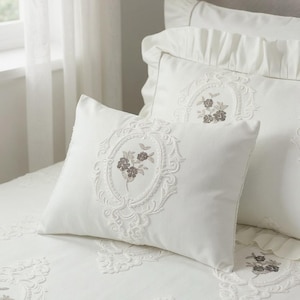 May include: White embroidered bedding set with floral designs. The set includes pillows and a duvet cover, in a soft, neutral colour palette. The embroidery features detailed floral patterns, adding a touch of elegance to the bedroom.