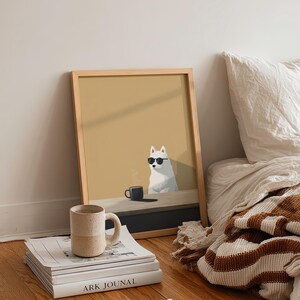 May include: A framed art print featuring a white dog wearing sunglasses, sitting at a table with a coffee cup. A stack of books and a speckled mug are in front of the print. The print is in a light wood frame. The word "moola" is in the bottom right corner.