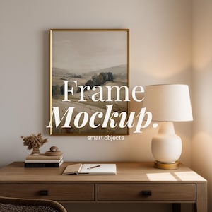 以下が含まれることがあります： 金色のフレームに入った風景画が木製の机の上に飾られています。 机にはランプ、本、ノートがあります。 テキスト「Frame Mockup. smart objects」が画像に重ねられています。