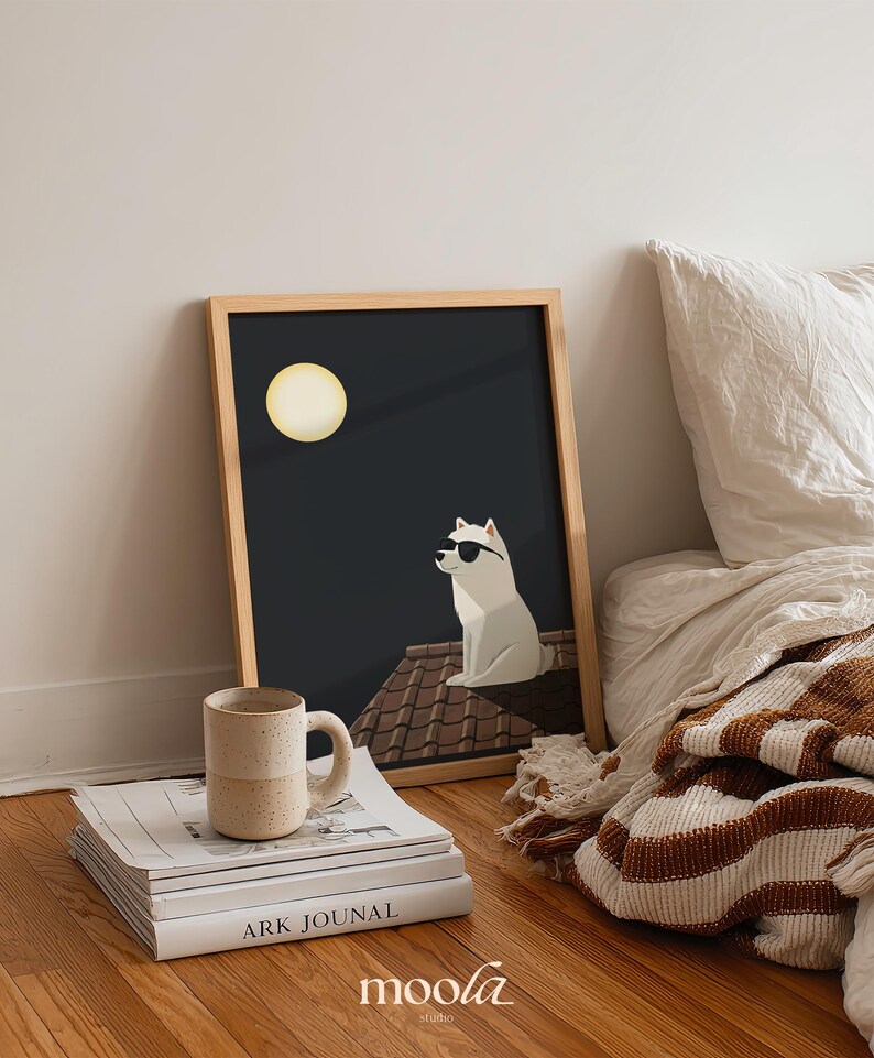 May include: A framed art print featuring a white dog wearing sunglasses, sitting on a rooftop under a full moon. A beige mug rests on a stack of books, with the text "ARK JOUNAL" visible. The artwork is set against a dark background.
