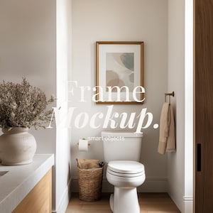May include: A bathroom interior with a white toilet, a framed artwork, and a woven basket. The artwork has a gold frame and abstract shapes in muted colors. The text "Frame Mockup. smart objects" is overlaid on the image.