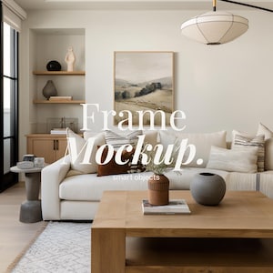 Puede incluir: Un salón moderno con un sofá blanco, una mesa de centro de madera y una pintura de paisaje enmarcada. Cojines y jarrones decorativos complementan la paleta de colores neutros. El texto "Frame Mockup" está presente.