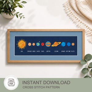 May include: A framed cross-stitch pattern featuring the Sun and planets of the solar system in pixel art style on a dark blue background. The text labels Sun, Mercury, Venus, Earth, Mars, Jupiter, Saturn, Uranus, Neptune, and Pluto appear below.