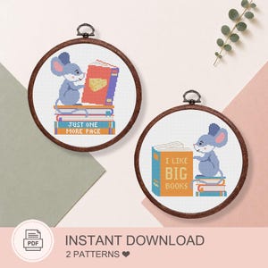May include: Two circular wooden embroidery hoops containing cross-stitch patterns of a blue mouse with books. One pattern shows a mouse on a stack of books with the text JUST ONE MORE PAGE. The other shows a mouse with a book labeled I LIKE BIG BOOKS.
