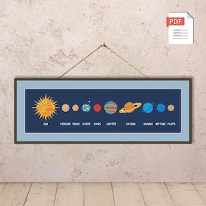 Può includere: Un ricamo a punto croce incorniciato che raffigura il sistema solare su uno sfondo blu scuro. Il sole è giallo brillante e i pianeti sono di vari colori. Il testo "SUN" e i nomi dei pianeti sono in basso. Un'icona PDF è in alto a destra.