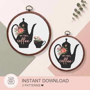 May include: Two circular wooden embroidery hoops containing cross-stitch patterns on white fabric. The designs feature a black silhouette of a coffee pot and cup adorned with pink roses and red berries, with the text "BUT FIRST, coffee" in pink.