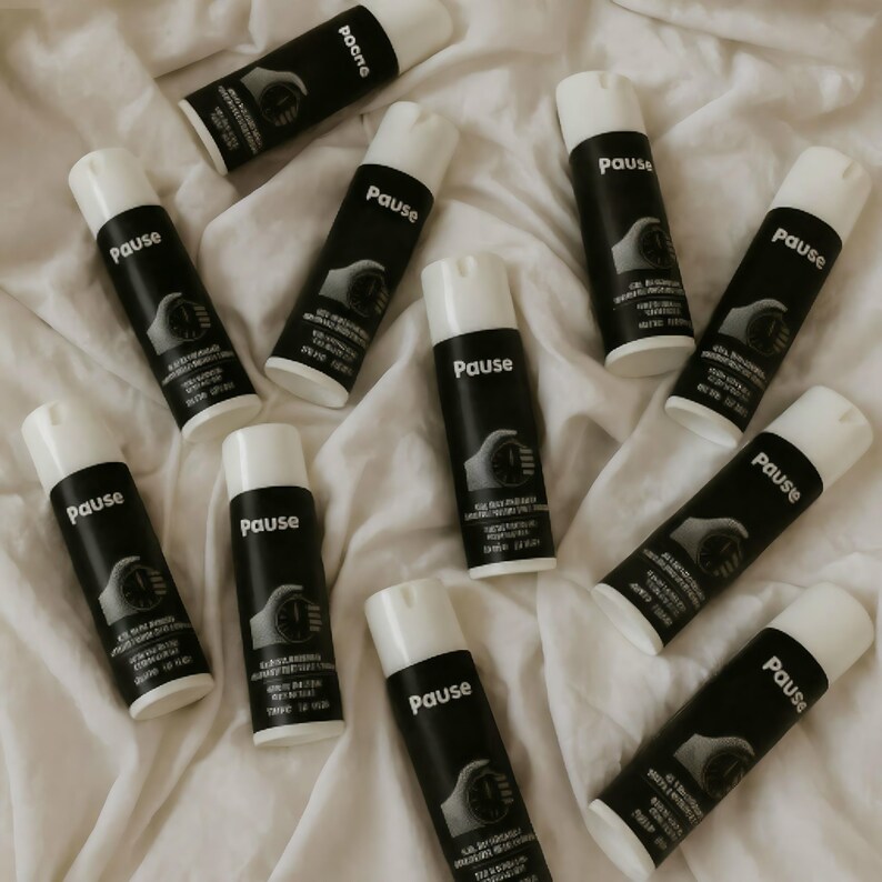 May include: A collection of black and white spray bottles, each labelled "Pause". The bottles have white caps and a graphic of a hand holding a stopwatch. They are arranged on a white, textured surface, creating a visually appealing display.