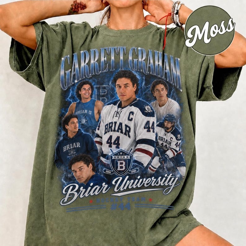May include: Olive green t-shirt featuring a graphic of a hockey player with the text "Garrett Graham" and "Briar University." The design includes multiple images of the player in various poses, with the number 44 prominently displayed on the jersey.