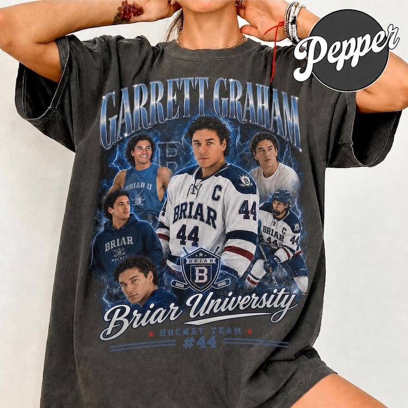 May include: Dark gray t-shirt featuring a graphic of Garrett Graham and the Briar University hockey team. The design includes multiple images of a hockey player, the text "Briar University Hockey Team #44", and lightning bolt accents.