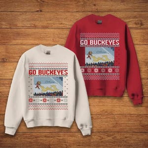 May include: Two sweatshirts with the text "GO BUCKEYES". One is cream-colored, the other is red. Both have a graphic of a running figure and a yellow shape, with red and white snowflake and zig-zag patterns.