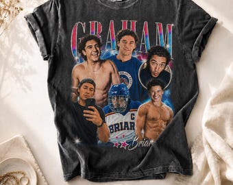 May include: Dark gray t-shirt featuring a collage of images with the name "GRAHAM" in a colorful, retro font. The shirt includes images of several people, with the name "Briar" and stars below.