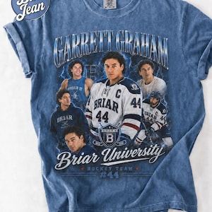 May include: Blue t-shirt featuring a graphic of Garrett Graham, Briar University Hockey Team #44. The design includes images of the player in various poses, with the team name and logo prominently displayed. The shirt has a vintage, faded look.