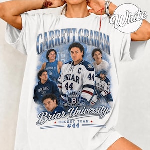 May include: White t-shirt featuring a graphic of Garrett Graham, a hockey player, with the text "Garrett Graham" and "Briar University Hockey Team #44". The design includes images of the player in various poses.