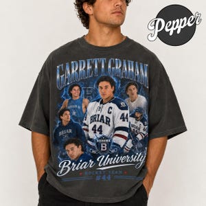 May include: Dark gray t-shirt featuring a graphic of Garrett Graham, Briar University hockey player. The design includes the text "Garrett Graham", "Briar University Hockey Team", and the number "44". The shirt has a vintage, distressed look.